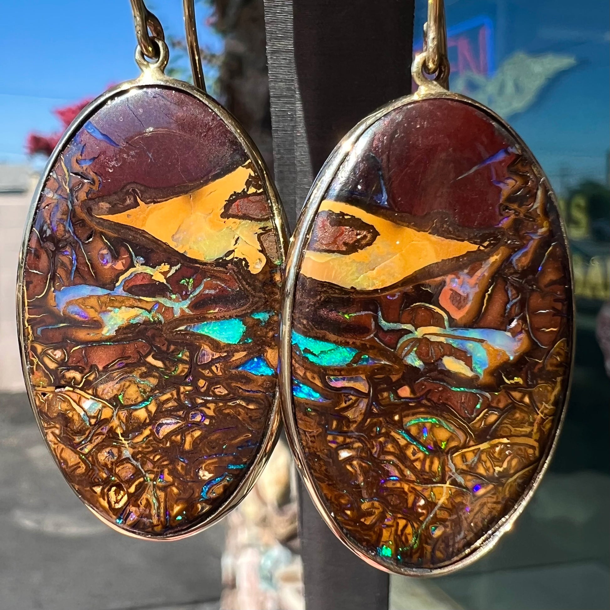 A pair of oval cut Koroit boulder opal dangle earrings in yellow gold bezel frames.  The opal exhibits a unique pattern and blue colors.