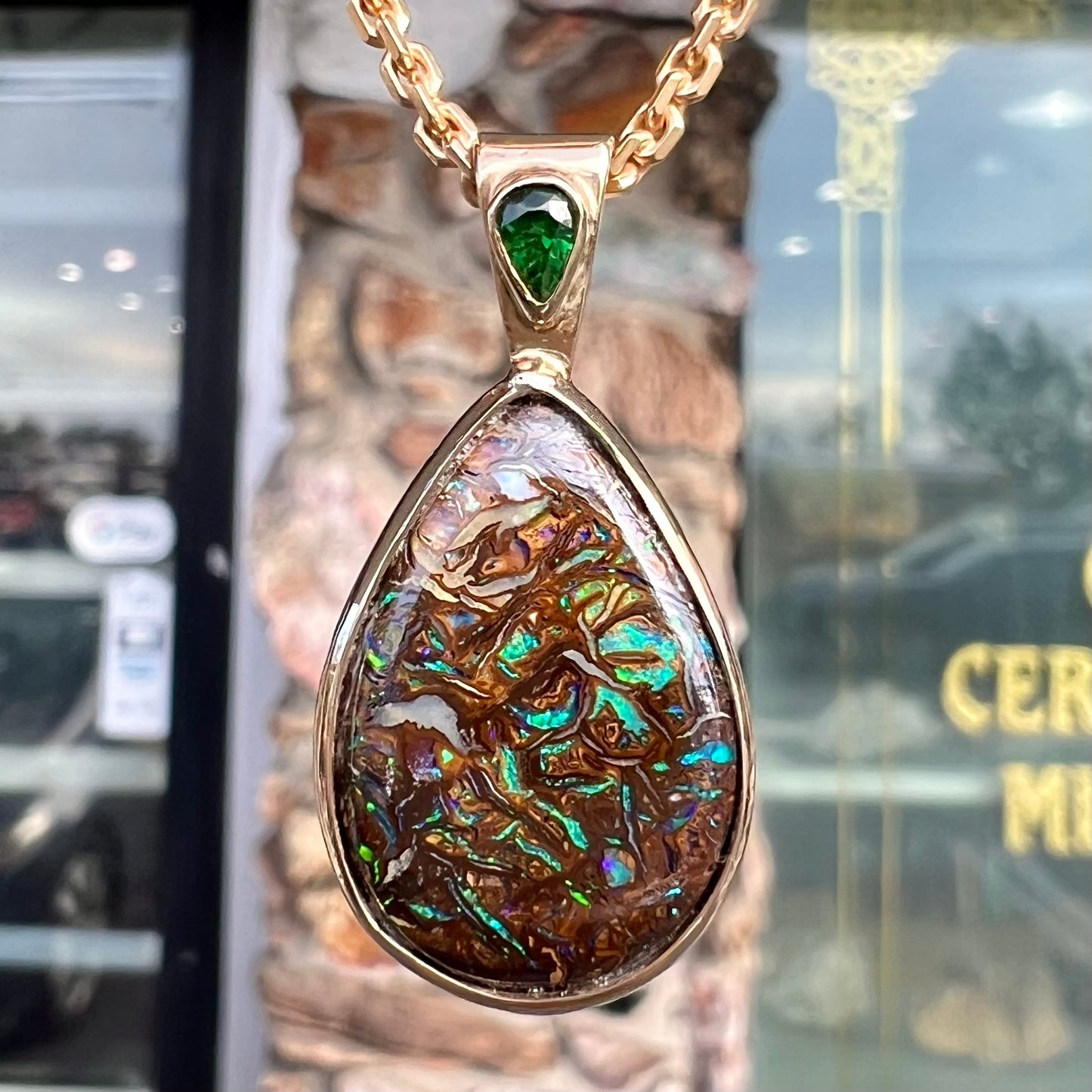 A ladies' yellow gold pendant set with a natural Koroit, Australian boulder opal and a tsavorite garnet accent stone.