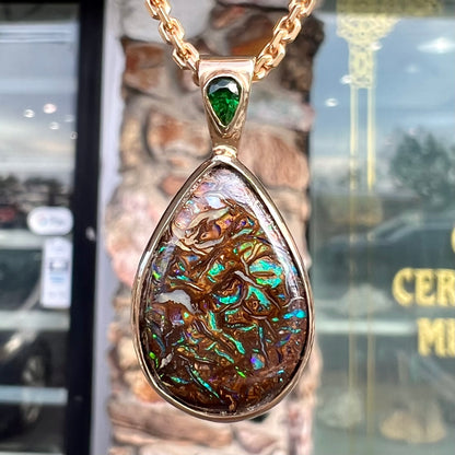 A ladies' yellow gold pendant set with a natural Koroit, Australian boulder opal and a tsavorite garnet accent stone.