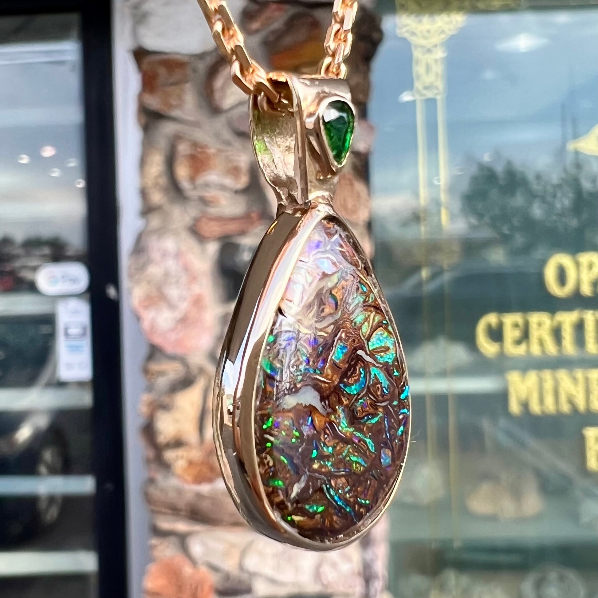 A ladies' yellow gold pendant set with a natural Koroit, Australian boulder opal and a tsavorite garnet accent stone.