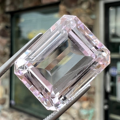 A loose, emerald cut kunzite gemstone.  The stone has eye-visible rutile needle inclusions and the table is abraded.