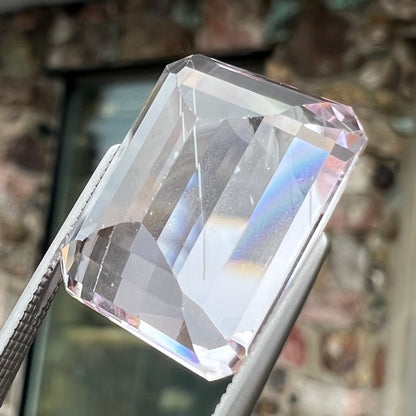 A loose, emerald cut kunzite gemstone.  The stone has eye-visible rutile needle inclusions and the table is abraded.