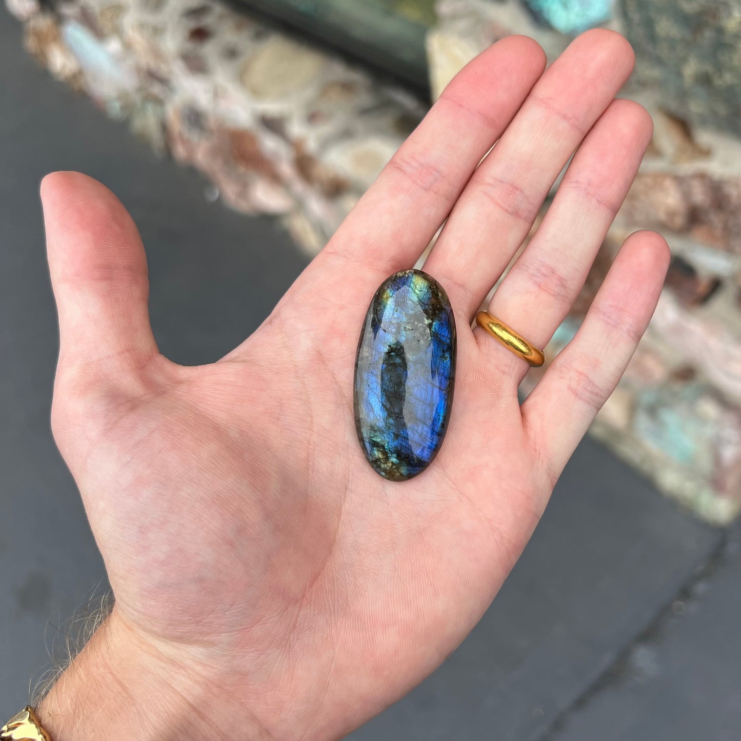 A loose, oval cabochon cut labradorite stone.  The stone is green with bright blue and yellow flashes.