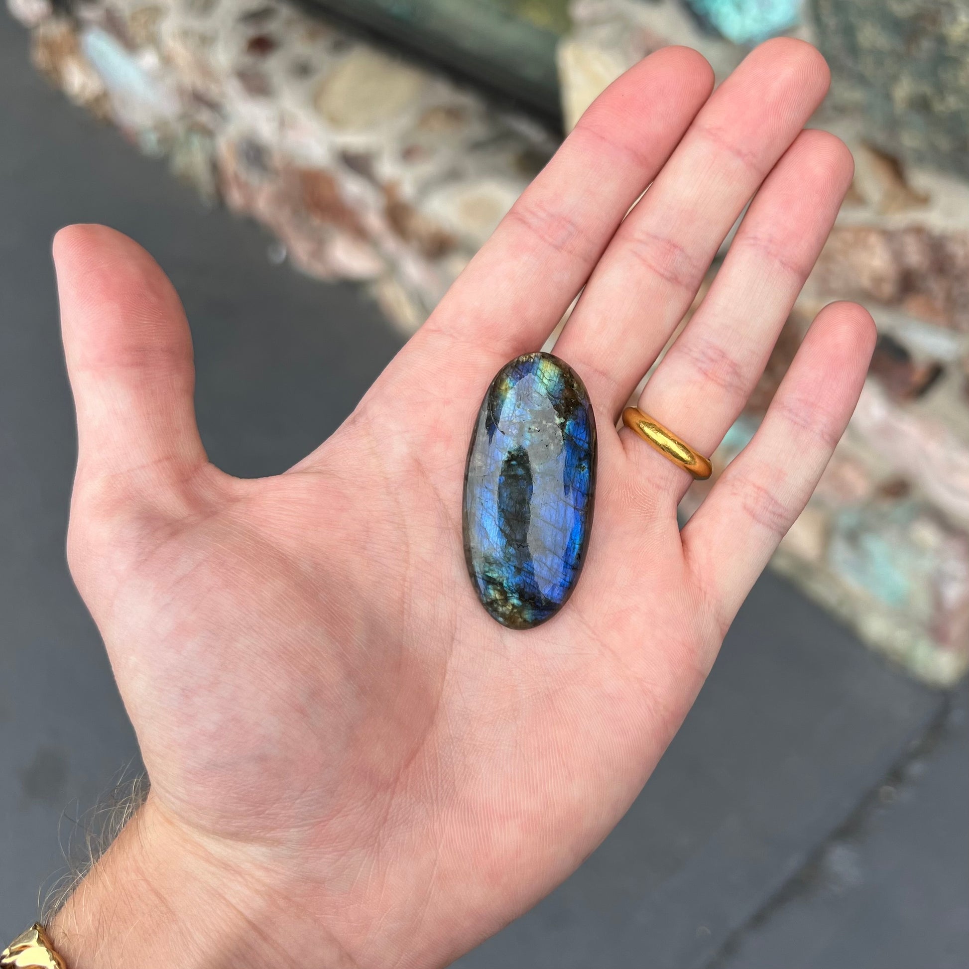 A loose, oval cabochon cut labradorite stone.  The stone is green with bright blue and yellow flashes.