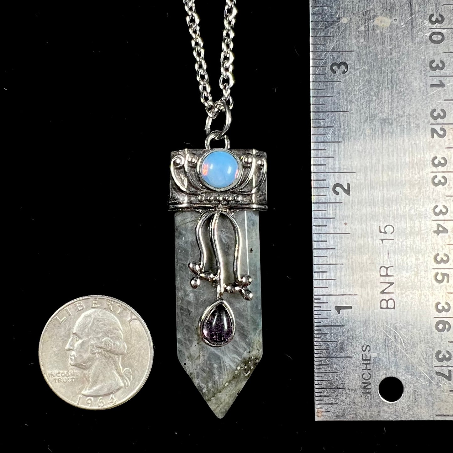 A stainless steal necklace set with a crystal shaped labradorite stone, purple glass, and an opalite accent.