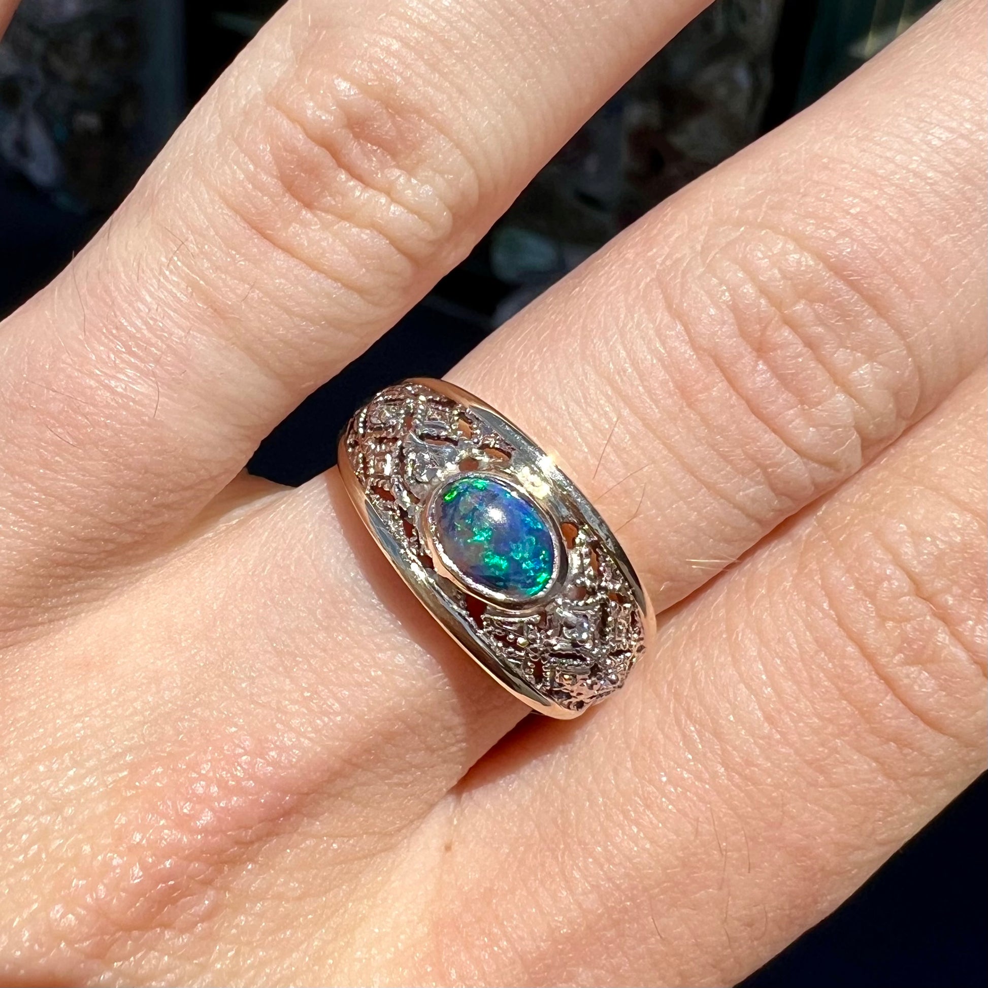 A ladies' yellow gold filigree style ring set with a natural black opal and diamond accents.