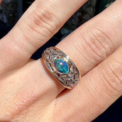 A ladies' yellow gold filigree style ring set with a natural black opal and diamond accents.