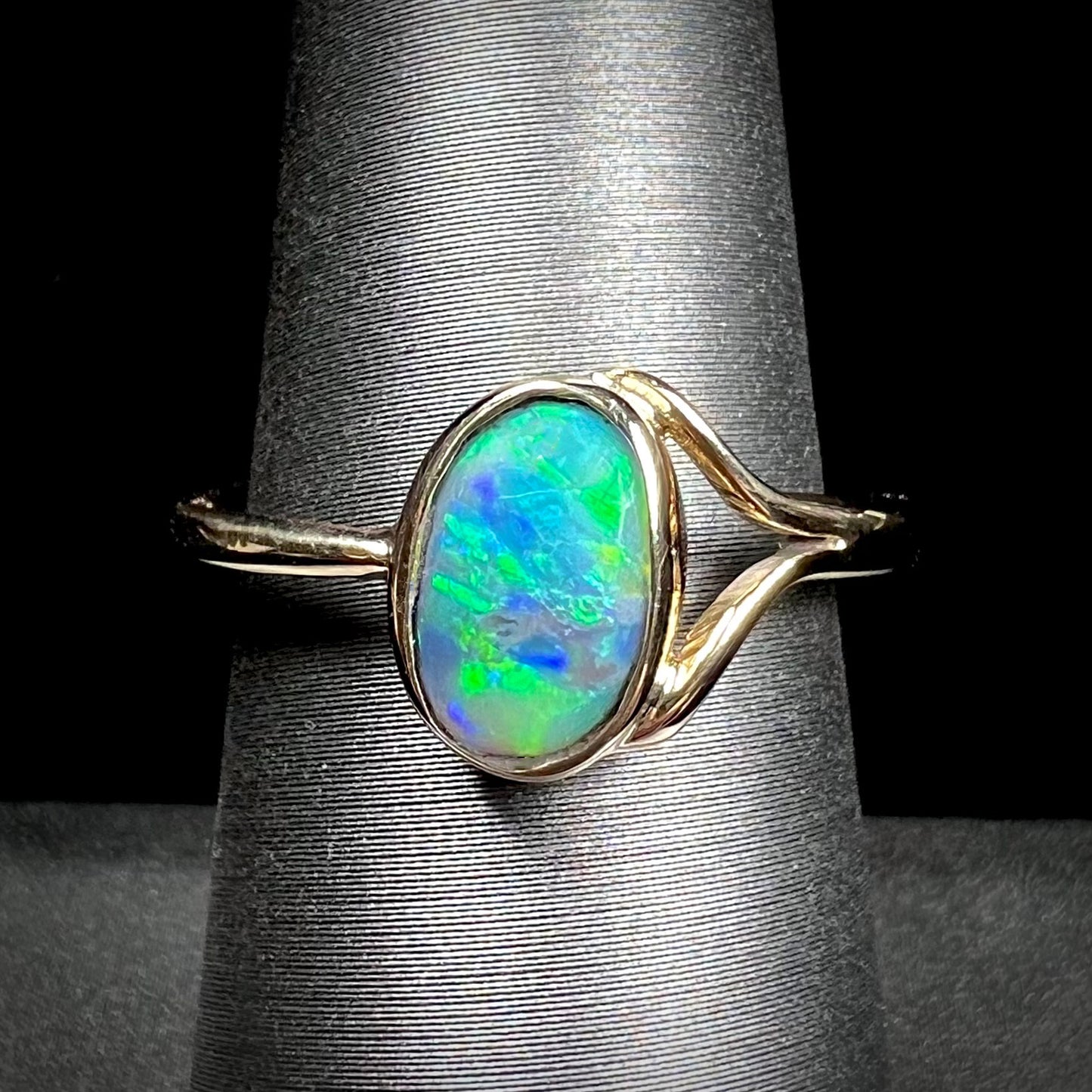 A ladies' oval cut black crystal opal solitaire ring handmade with a single split shank in yellow gold.