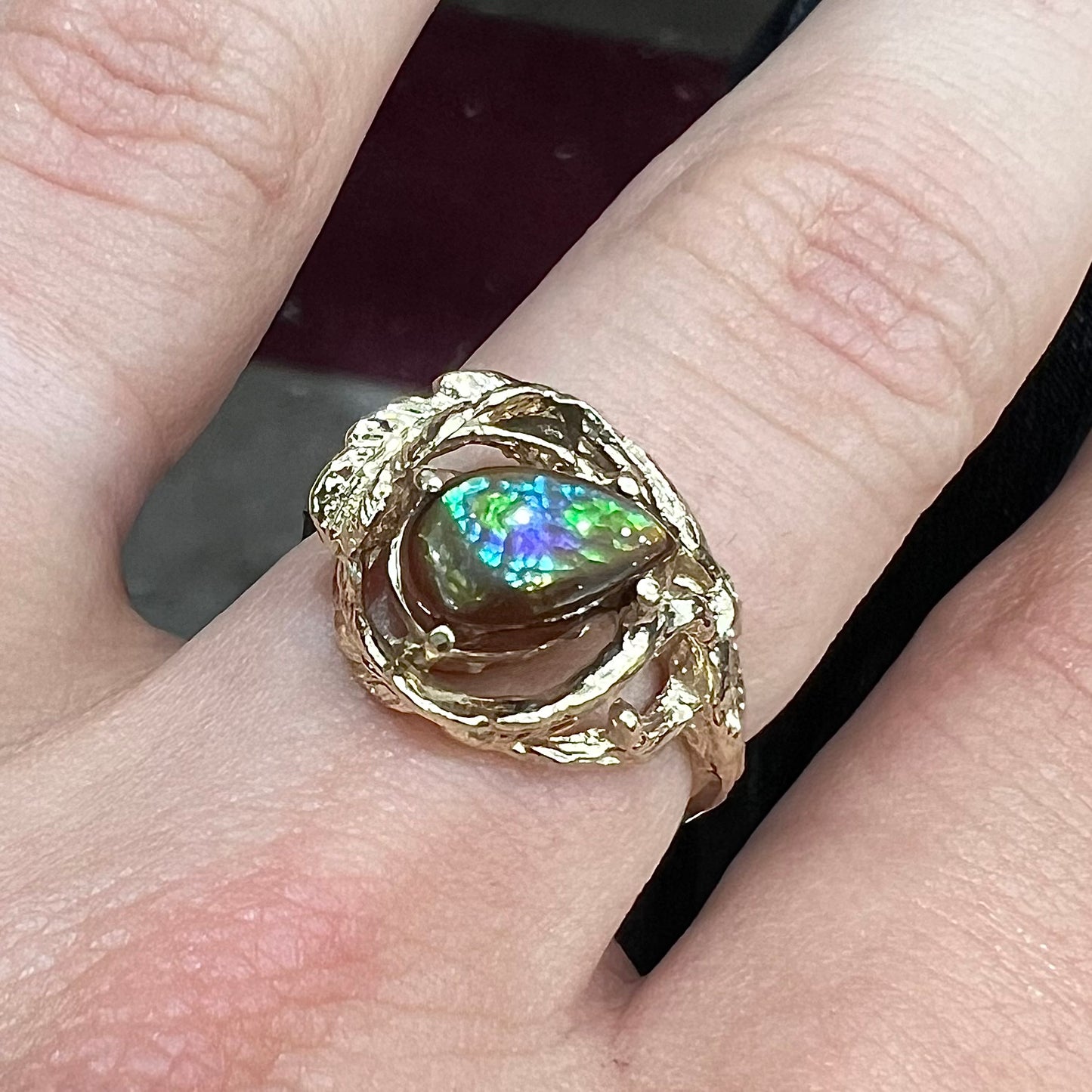 A ladies' organic style yellow gold ring set with a pear shaped cabochon cut Mexican fire agate.  The stone shines green and purple.