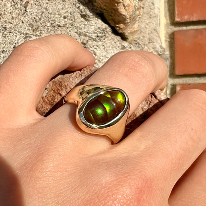 A yellow gold unisex Mexican fire agate solitaire ring.  The stone exhibits a snakeskin pattern with green, yellow, orange, and blue colors.