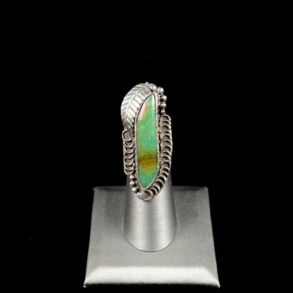 A sterling silver Navajo style ring set with a turquoise stone that shows colors of green, yellow, and reddish brown.