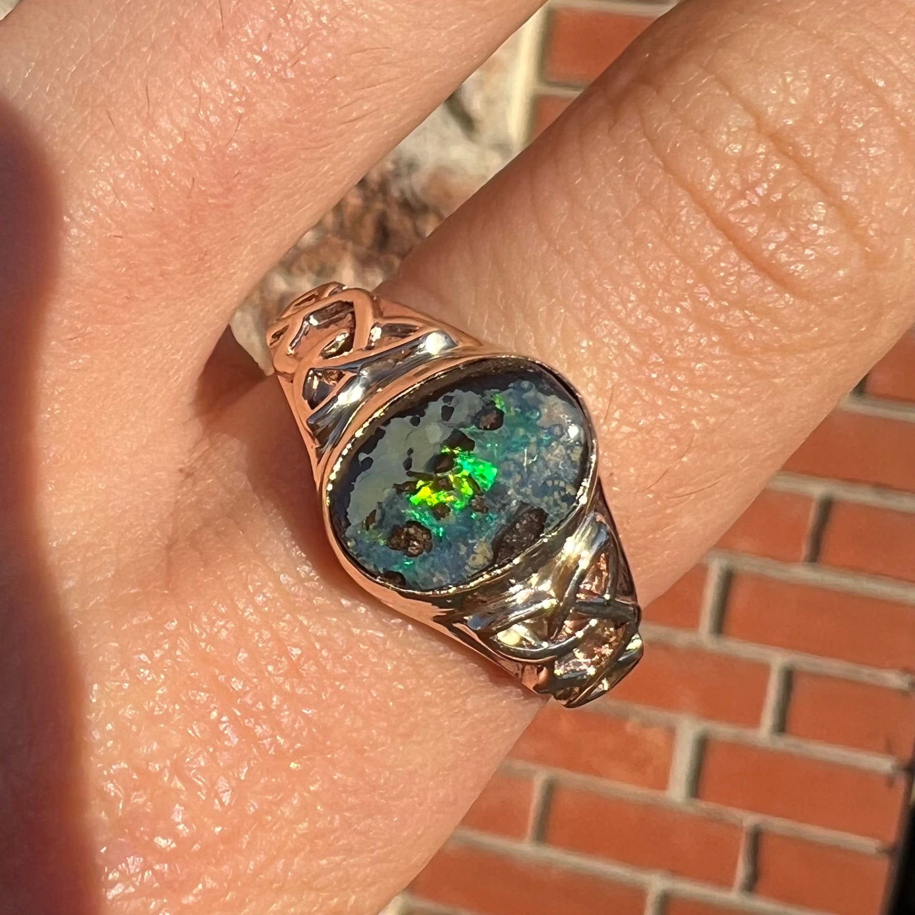 A unisex Celtic style natural boulder opal ring cast in yellow gold.  The opal shines green and blue.