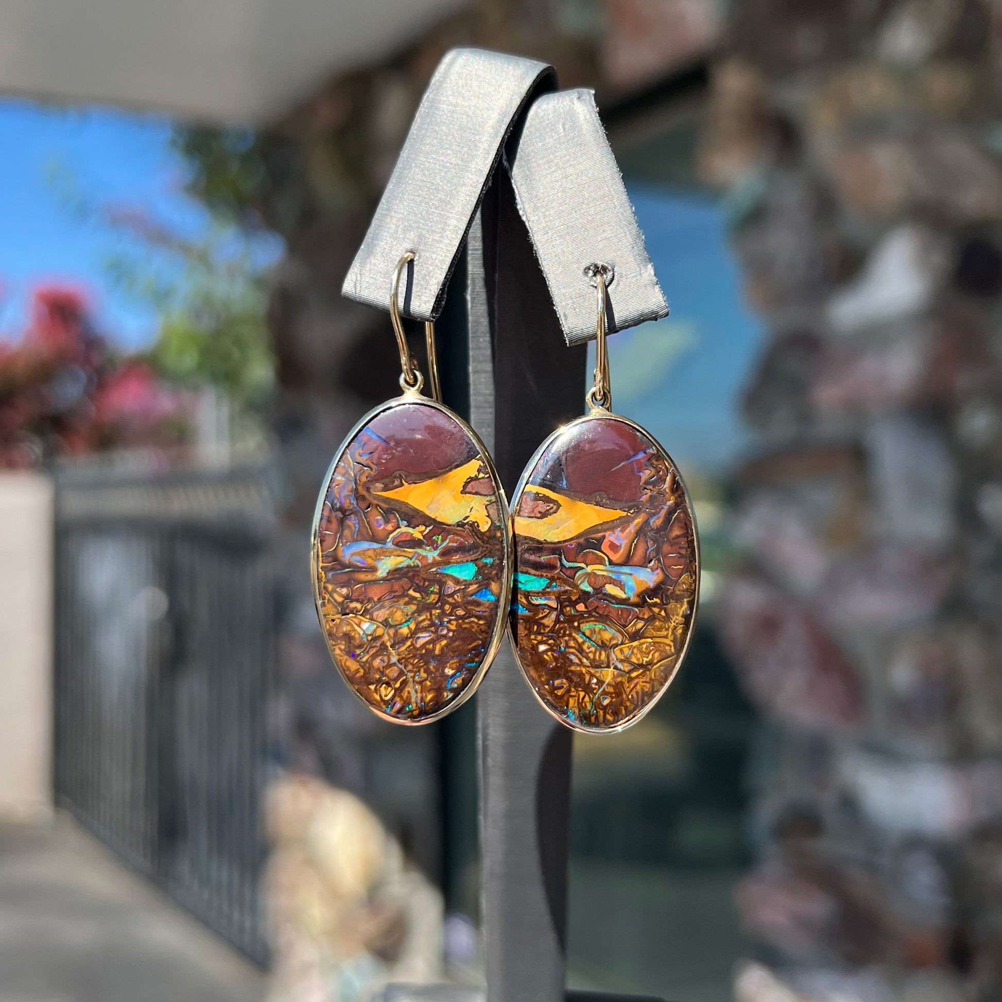 A pair of oval cut Koroit boulder opal dangle earrings in yellow gold bezel frames.  The opal exhibits a unique pattern and blue colors.