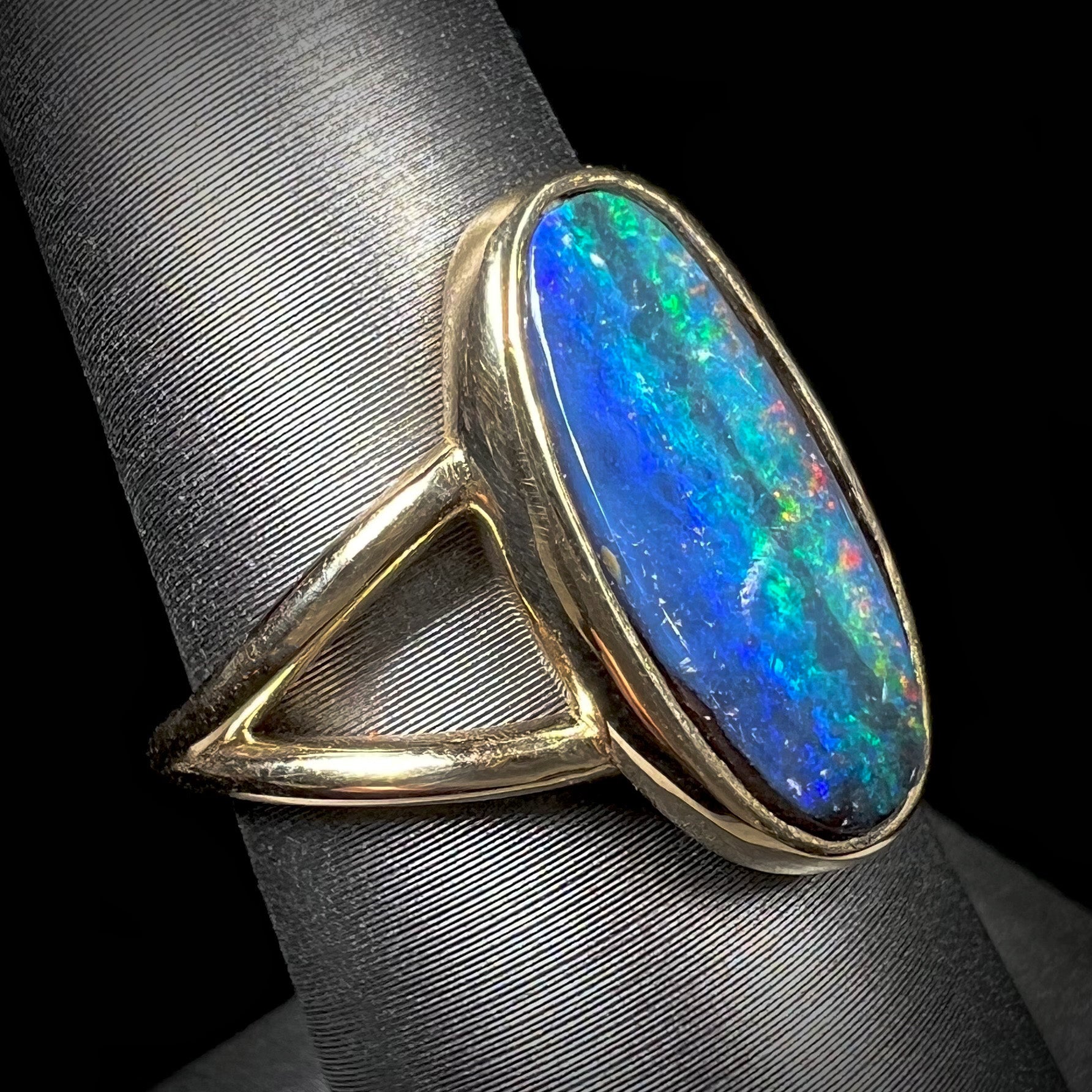 A ladies' yellow gold split shank solitaire ring set with a natural Australian black boulder opal.