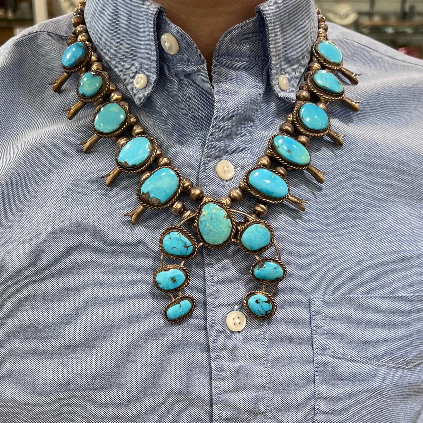 A sterling silver, Navajo style squash blossom necklace set with Morenci turquoise stones.  The legnth is designed for women and children.