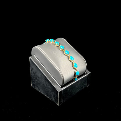 A ladies' yellow gold tennis style bracelet set with pear cabochon shaped natural Sleeping Beauty turquoise stones.
