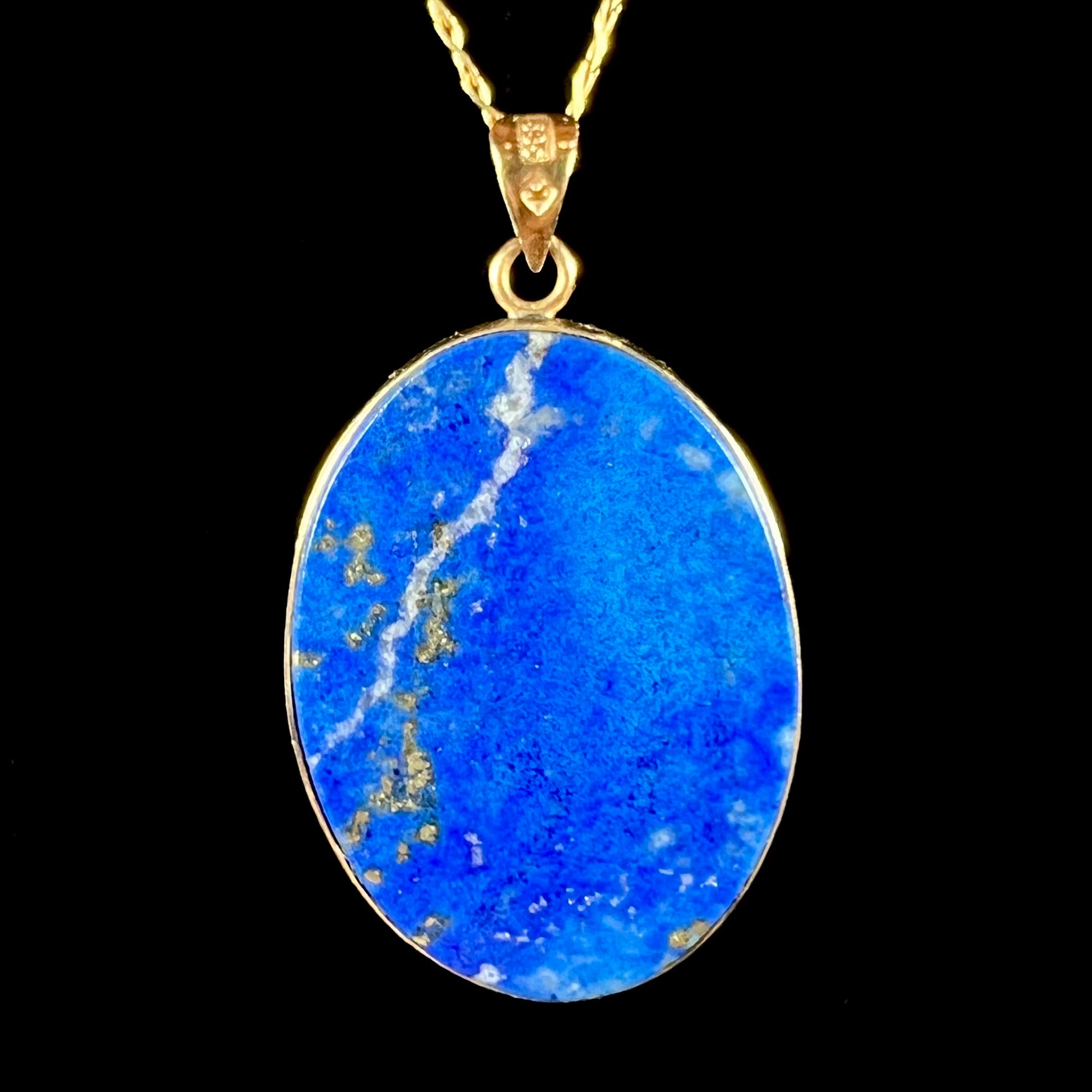 An oval cut lapis lazuli pendant set in a yellow gold frame featuring the design of two swans swimming in a pond.