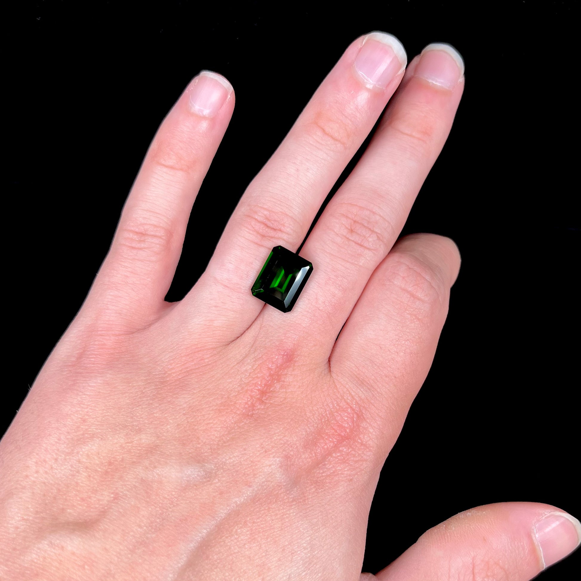 A large, emerald cut chrome diopside gemstone.  The gem is dark green color.
