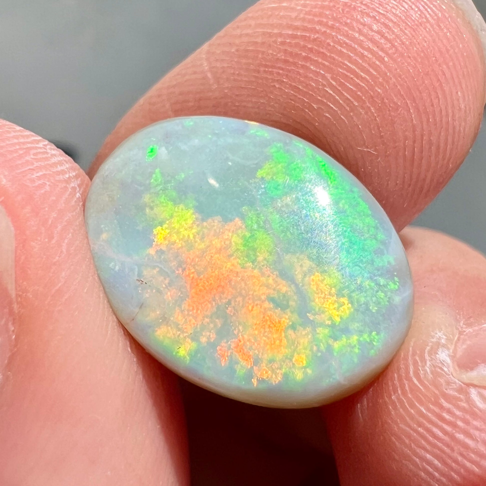 A loose, oval cut light opal stone from Mintabie, Australia.  The stone shows dull orange and green colors.