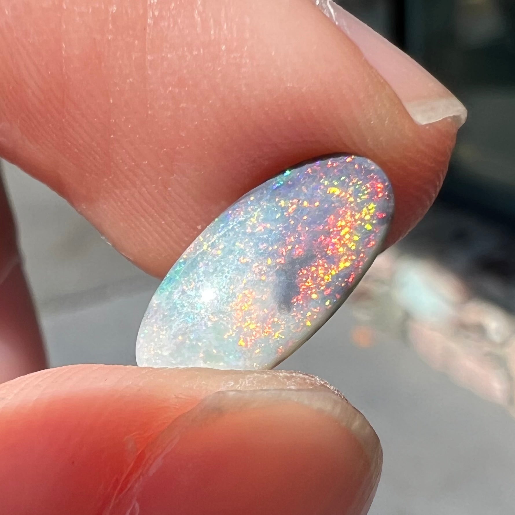 A loose, oval cabochon cut opal gemstone from Lightning Ridge, Australia.  The opal shines red and orange colors.