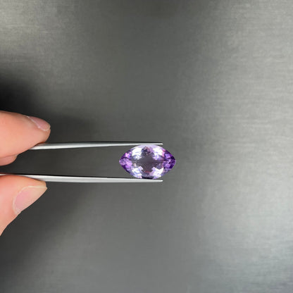 A loose marquise cut amethyst gemstone.  The stone is a light purple color and has scratches along the surface.
