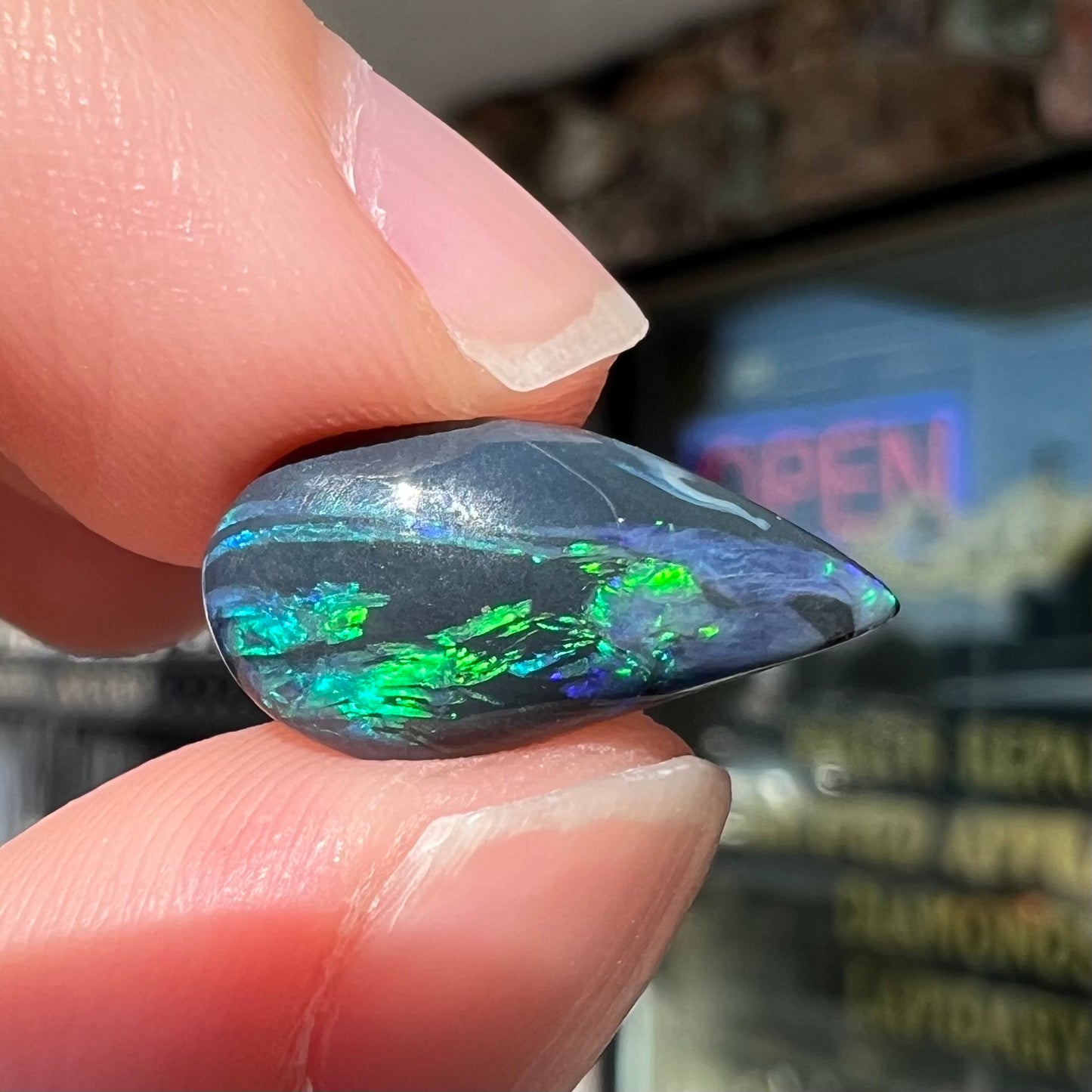 A freeform pear shaped black opal from Lightning Ridge, Australia.  The opal has green fire.