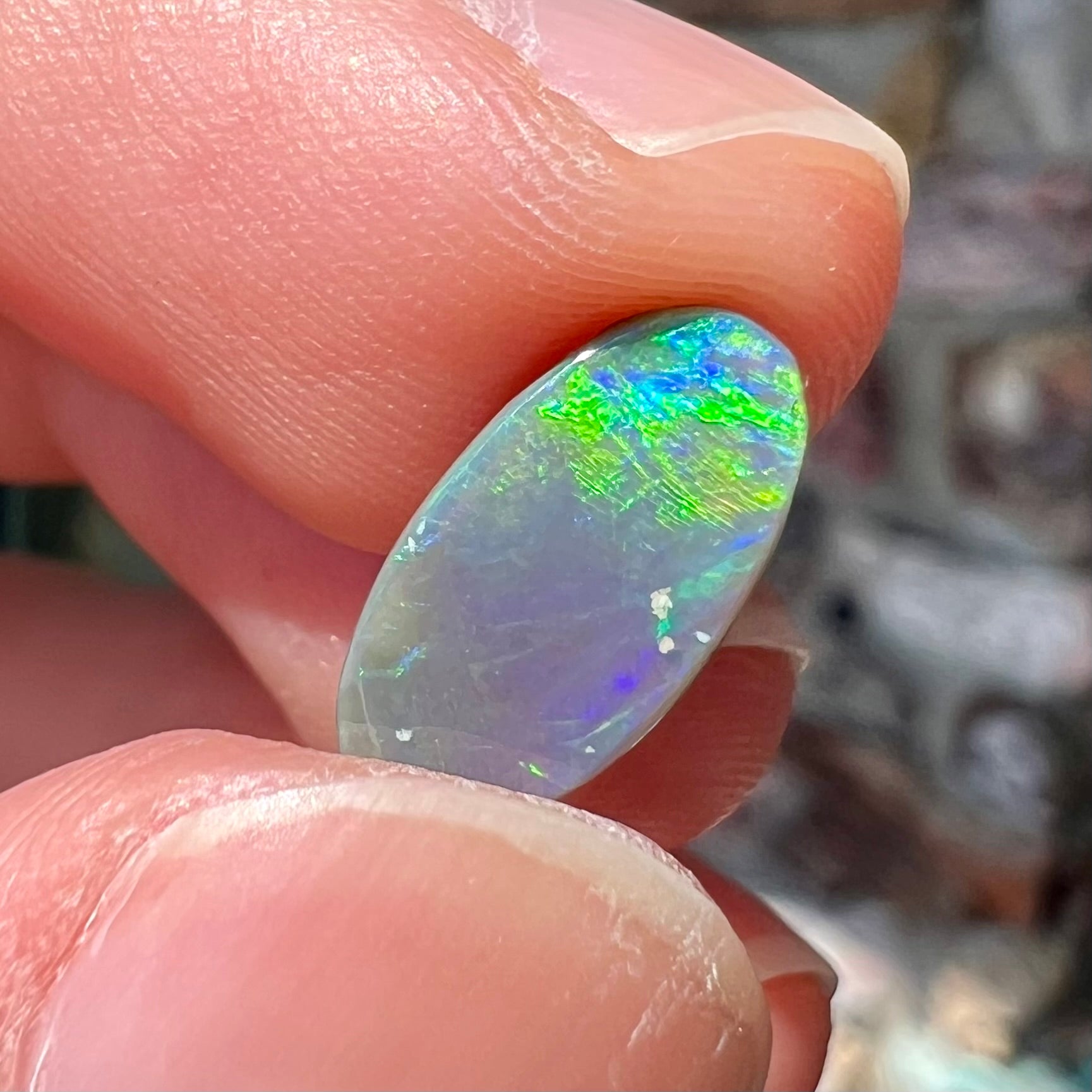 A loose, oval shaped black opal stone from Lightning Ridge, Australia.  The opal plays bright green and blue colors.