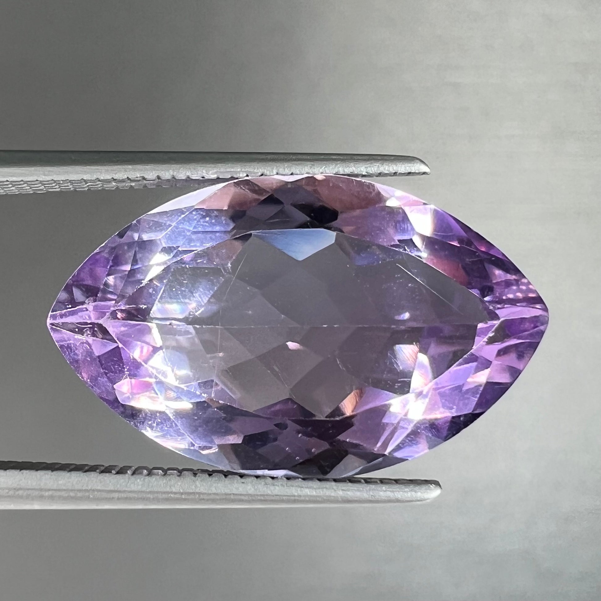 A loose marquise cut amethyst gemstone.  The stone is a light purple color and has scratches along the surface.