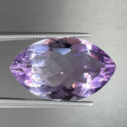 A loose marquise cut amethyst gemstone.  The stone is a light purple color and has scratches along the surface.