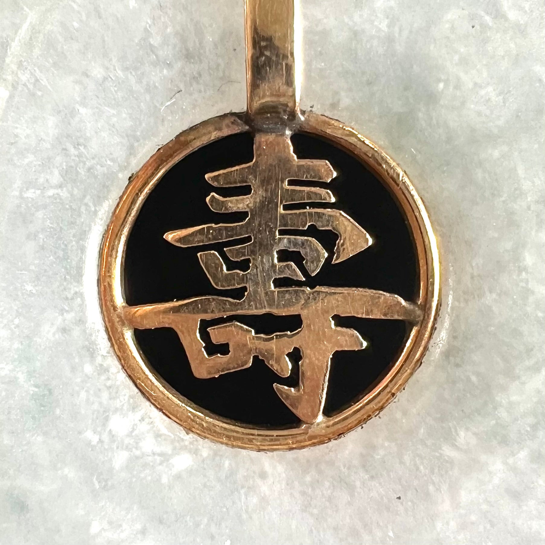 A light green jadeite jade bi pendant with a yellow gold bail and Chinese character symbol for "long life."