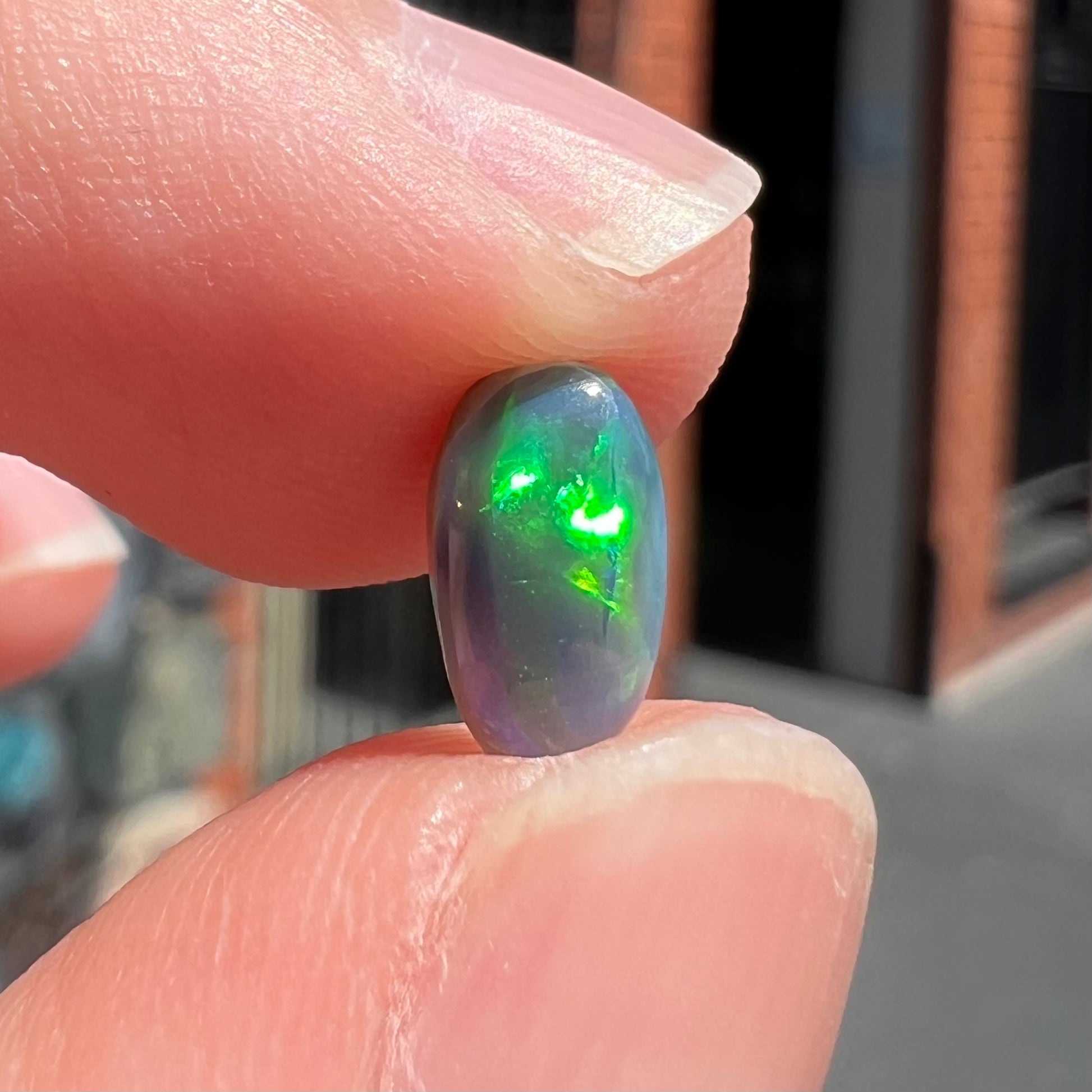 A loose, pill shaped black opal stone from Lightning Ridge, Australia.  The opal is green and blue.