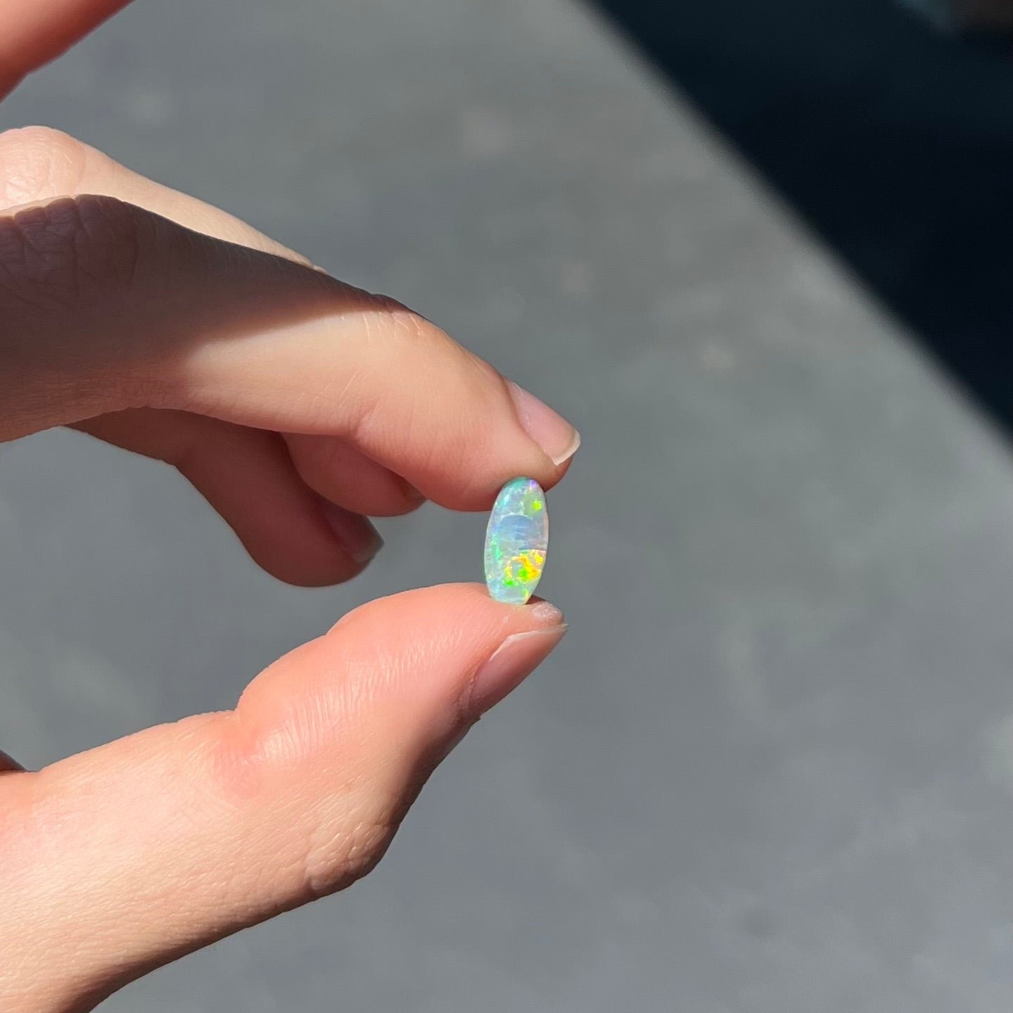 A loose, oval cabochon cut semi-black opal from Lightning Ridge, Australia.  The opal plays green and orange colors.