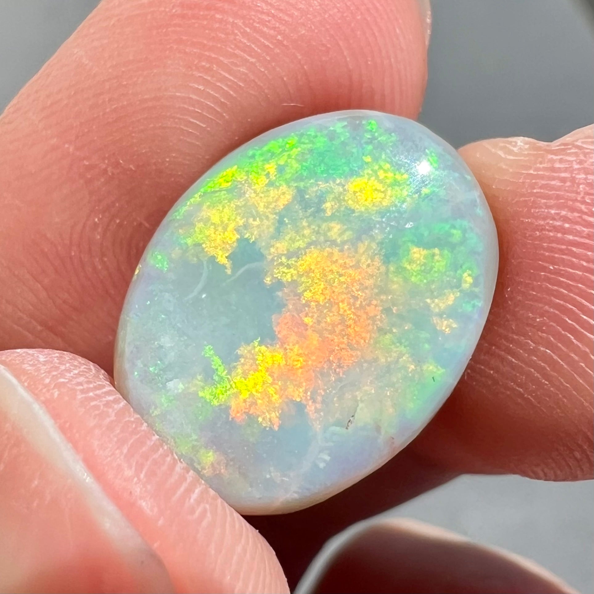 A loose, oval cut light opal stone from Mintabie, Australia.  The stone shows dull orange and green colors.