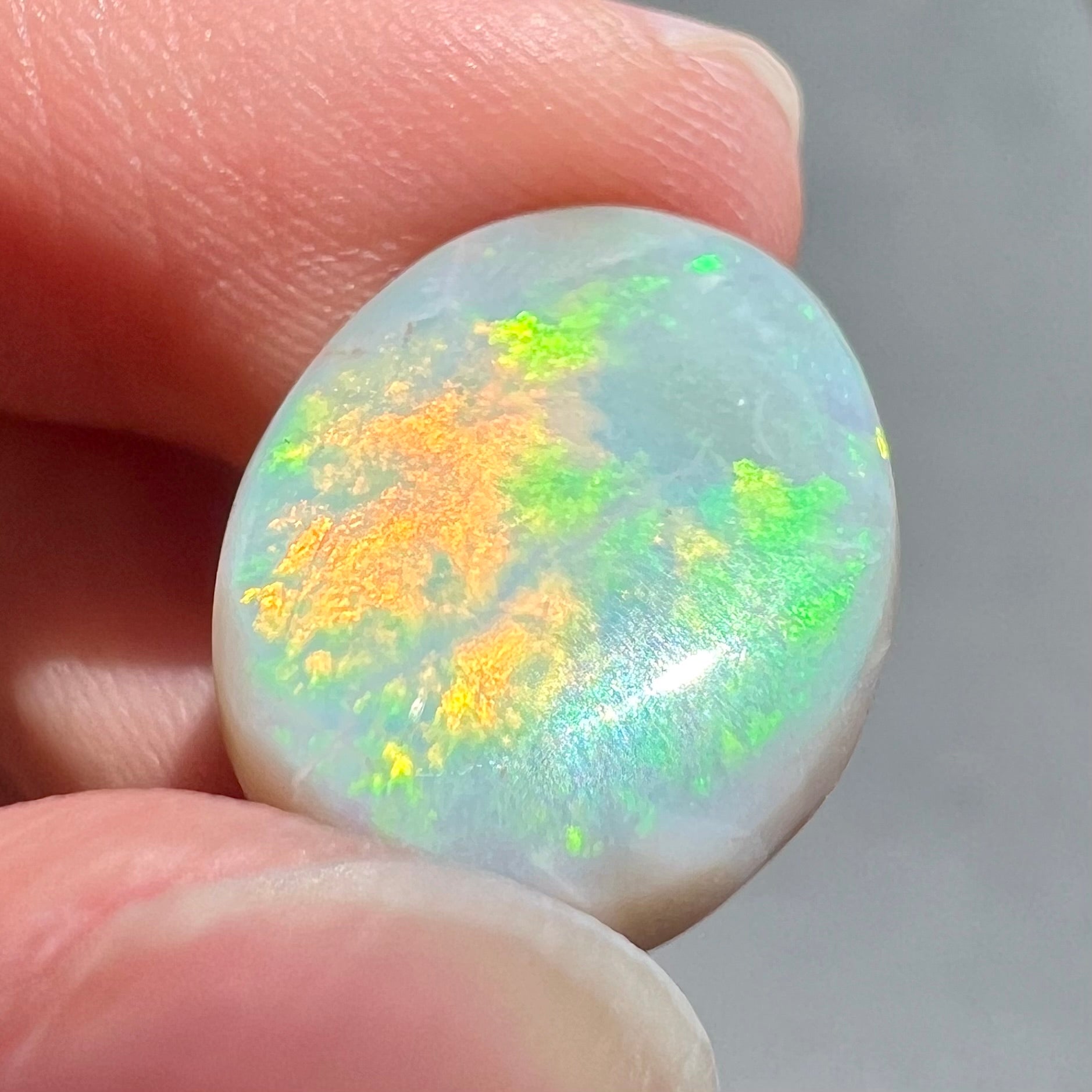 A loose, oval cut light opal stone from Mintabie, Australia.  The stone shows dull orange and green colors.