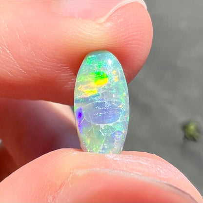 A loose, oval cabochon cut semi-black opal from Lightning Ridge, Australia.  The opal plays green and orange colors.