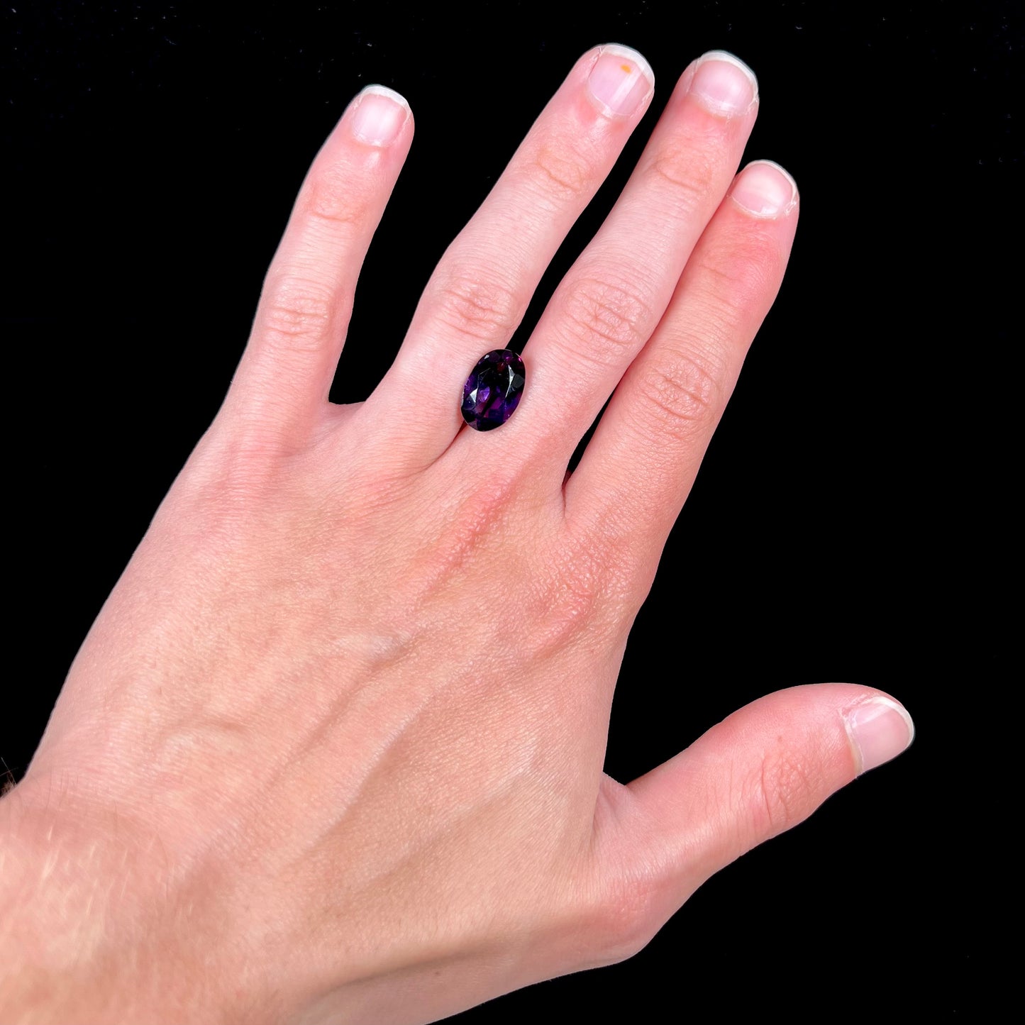 A loose, faceted oval cut Siberian amethyst gemstone.  The stone is purple color with blue and red flashes.