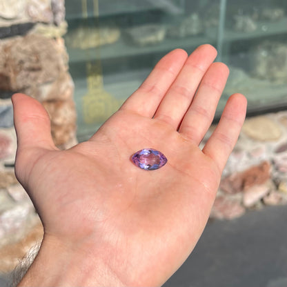 A loose marquise cut amethyst gemstone.  The stone is a light purple color and has scratches along the surface.