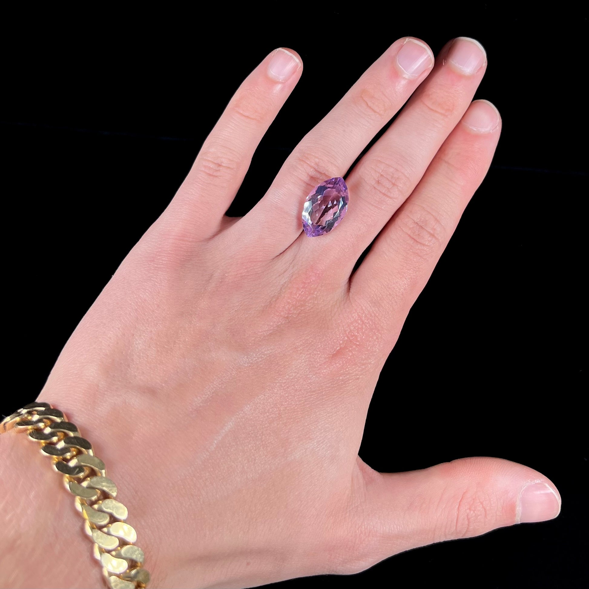 A loose marquise cut amethyst gemstone.  The stone is a light purple color and has scratches along the surface.