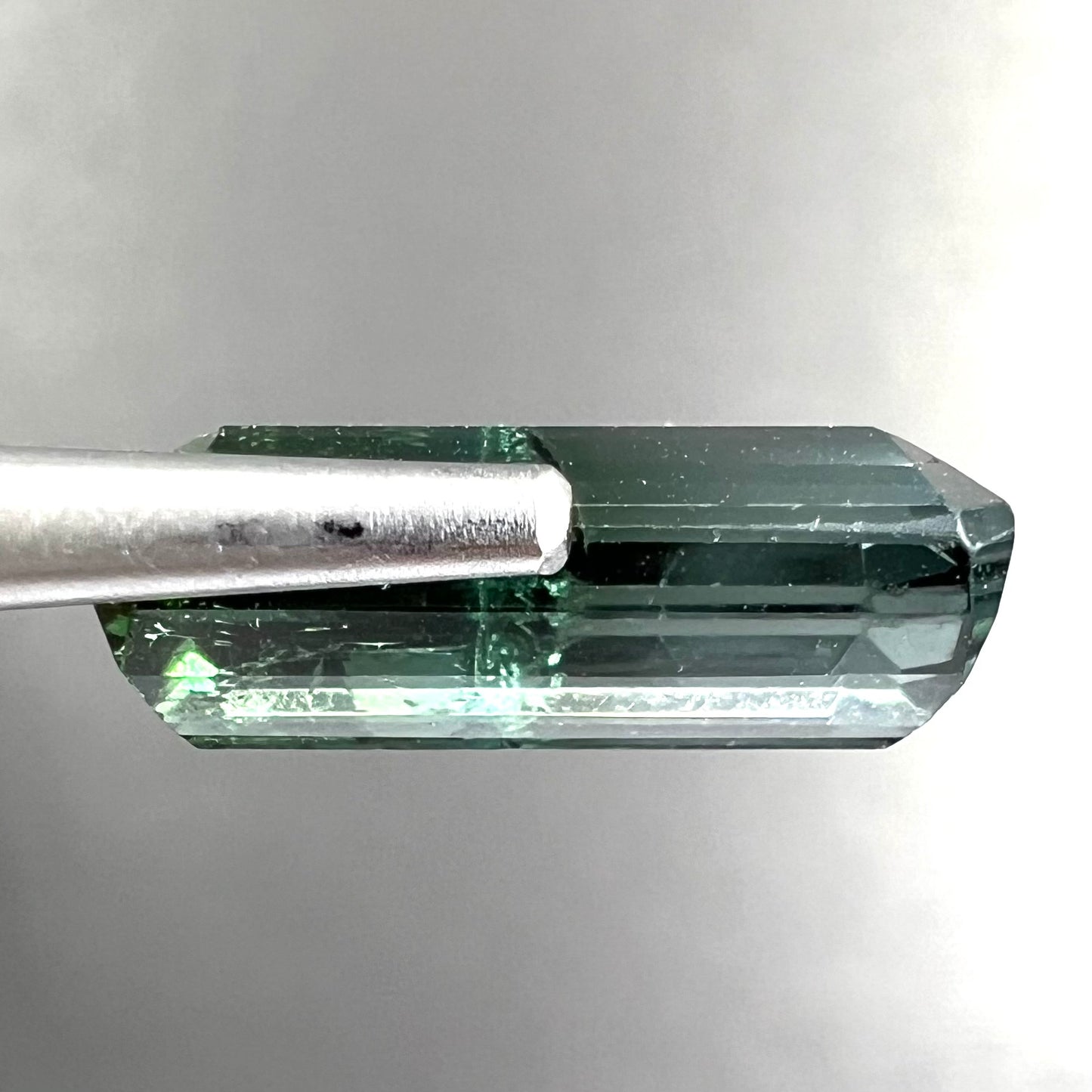 A loose, emerald cut bicolor tourmaline stone.  The colors blend from green to blue-green to sttel blue.