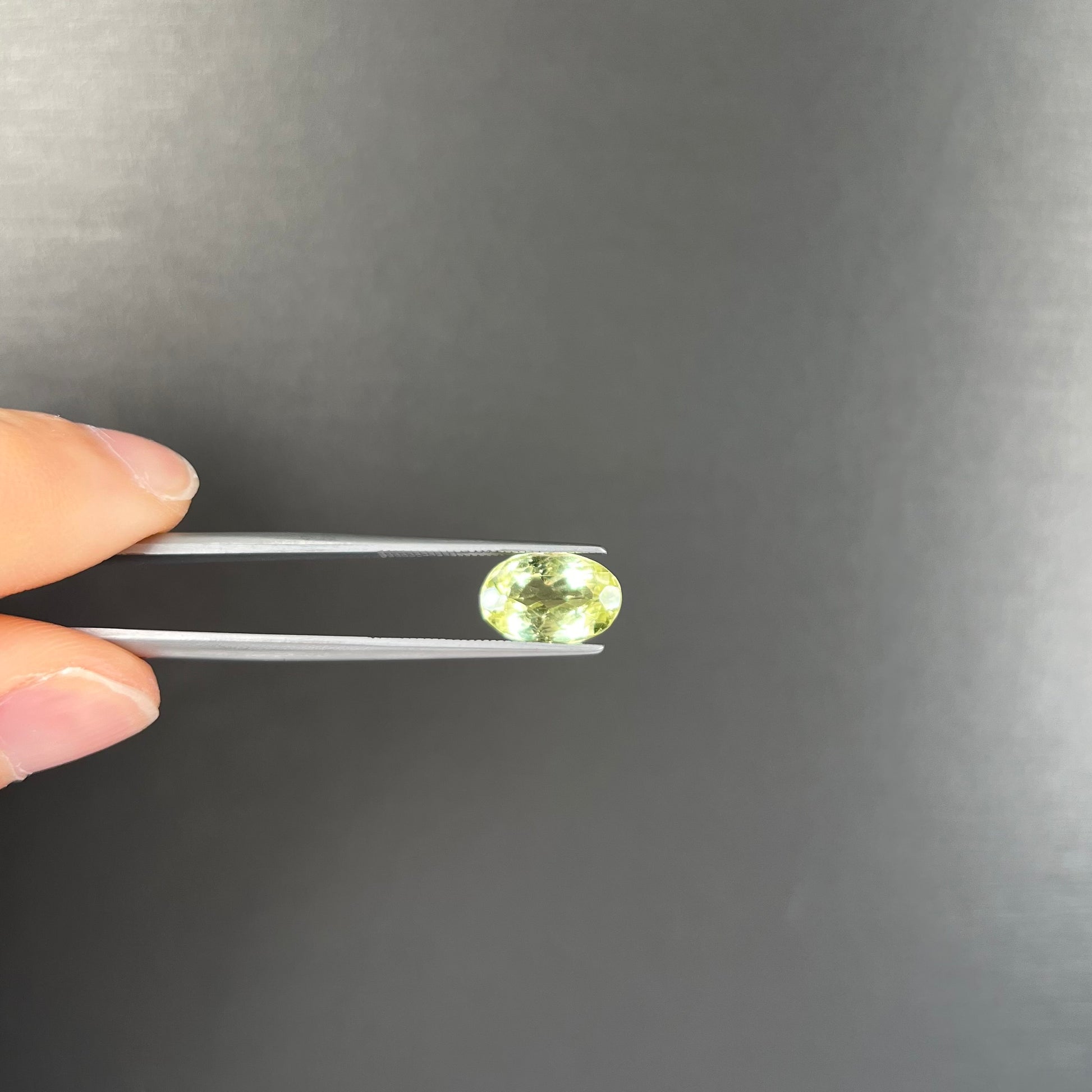 A loose, faceted oval cut chrysoberyl gemstone.  The stone is a greenish yellow color.