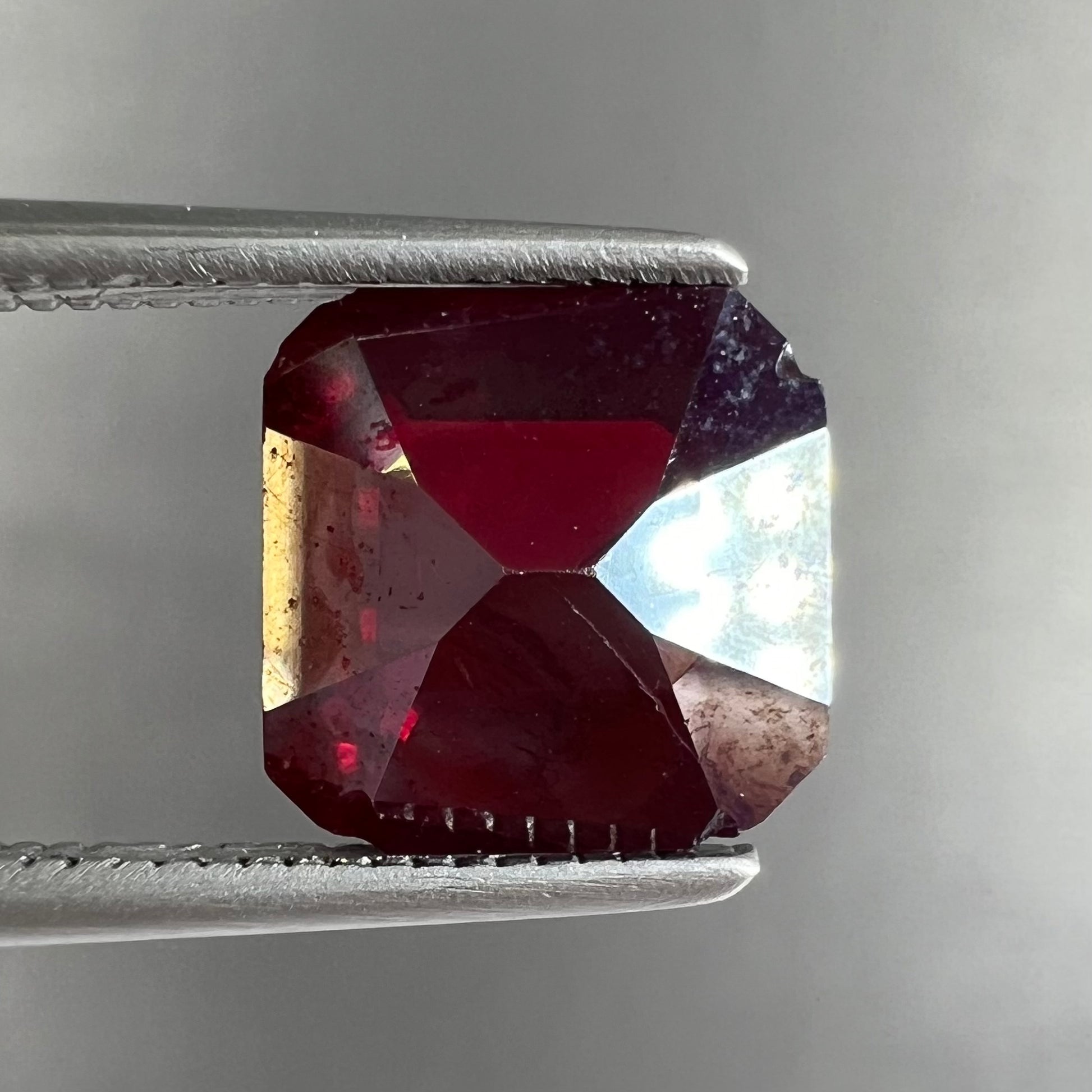 A loose, modified Asscher cut cuprite gemstone.  The stone is a deep, crimson red color and has several chips along the girdle.