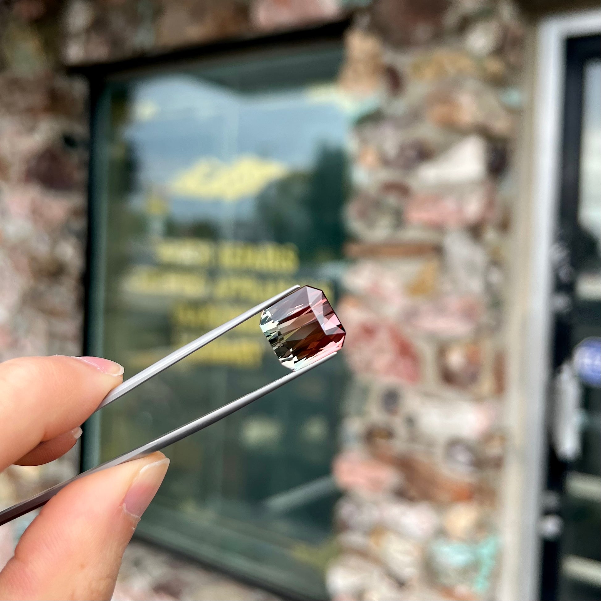 A loose, faceted modified emerald cut bicolor tourmaline gemstone.  The stone transitions from dark pink to dark green colors.