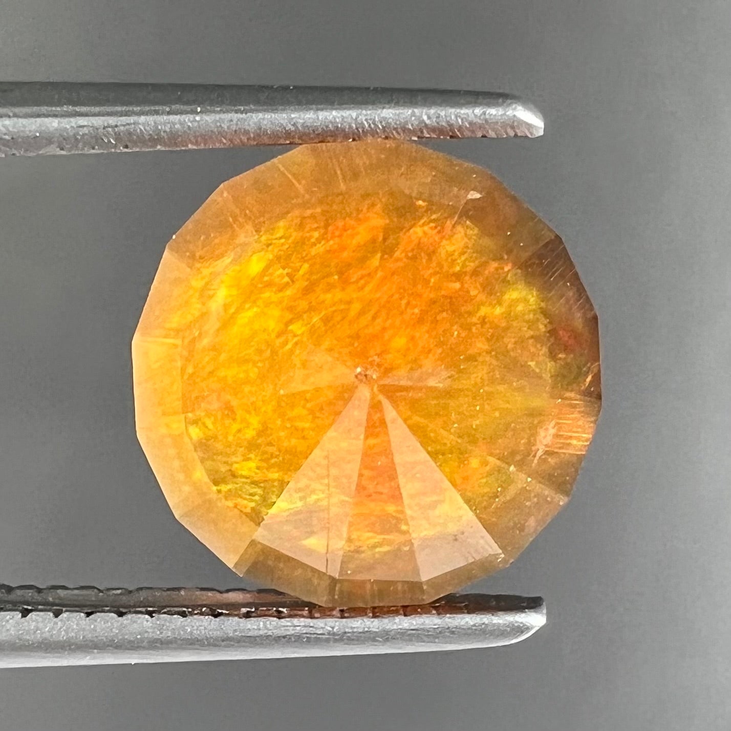A loose, round faceted cut fire opal from Mexico.  The body color is yellowish orange with red, green, and yellow fire.
