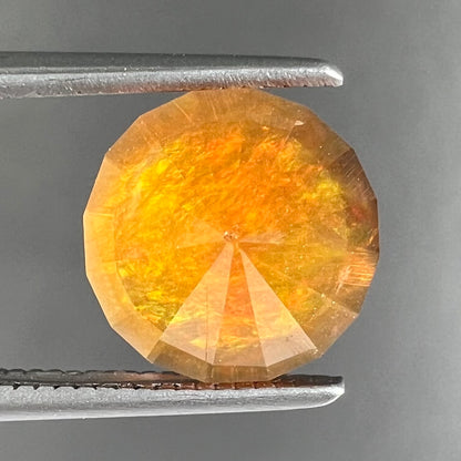 A loose, round faceted cut fire opal from Mexico.  The body color is yellowish orange with red, green, and yellow fire.