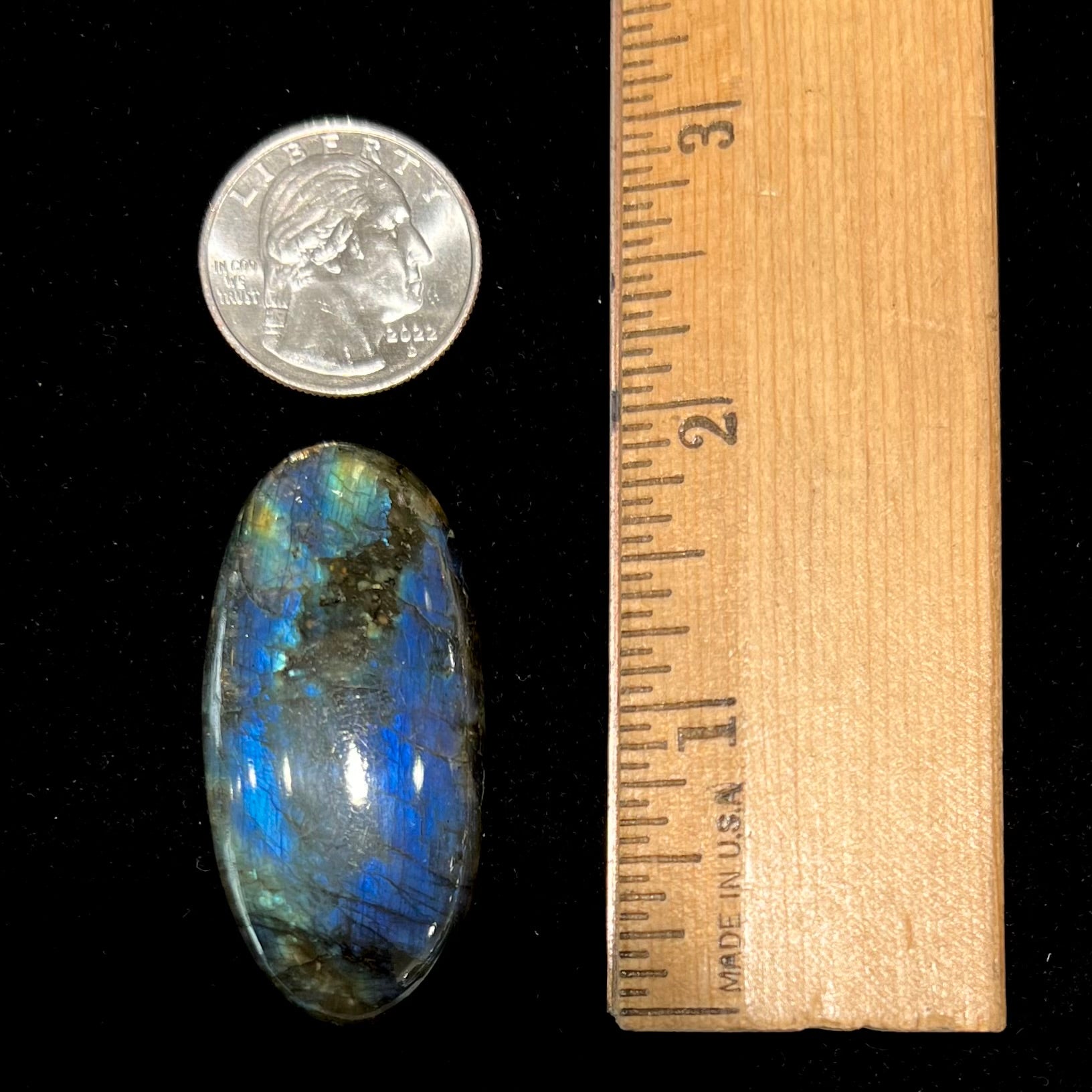 A loose, oval cabochon cut labradorite stone.  The stone is green with bright blue and yellow flashes.