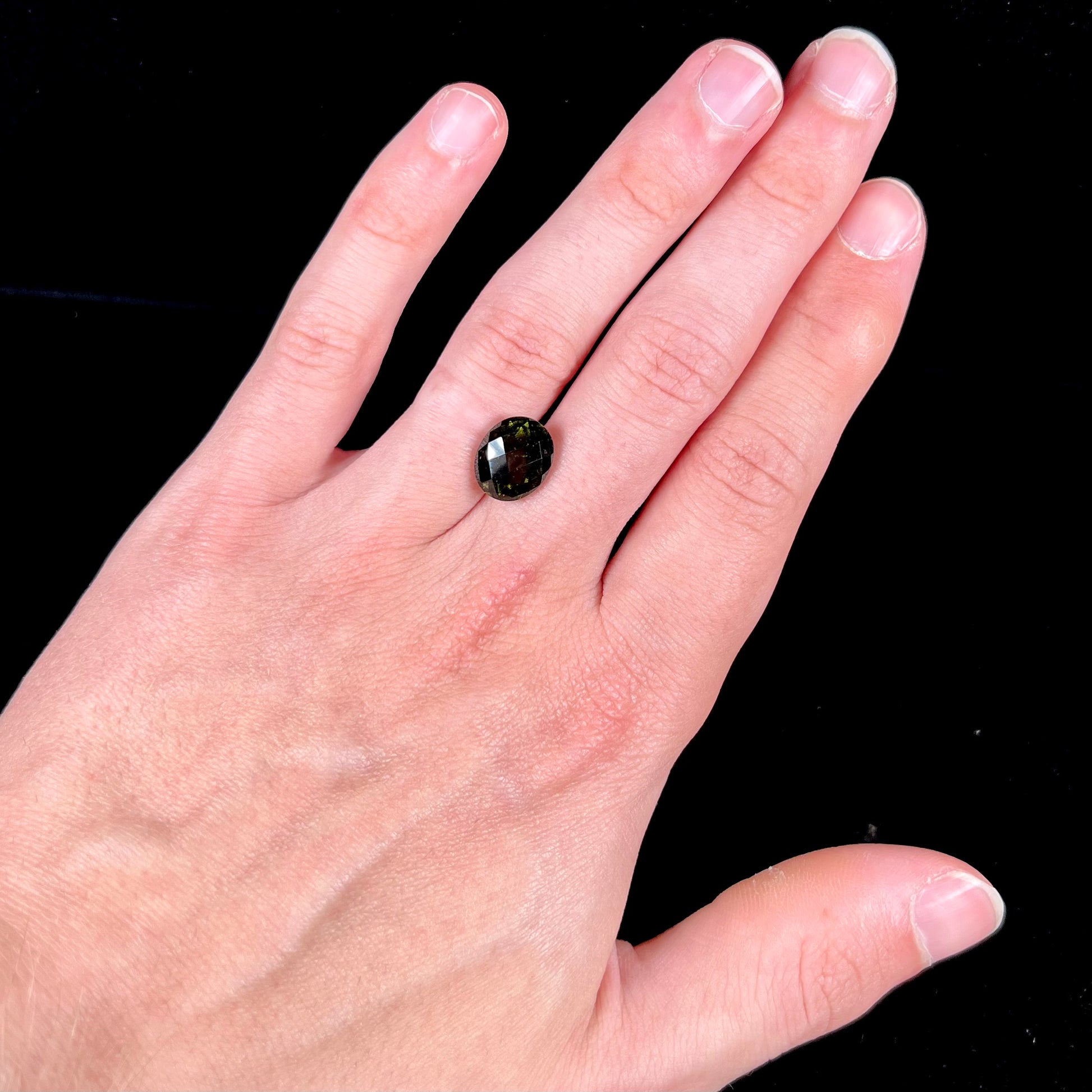 A loose, faceted oval cut natural moldavite gemstone.