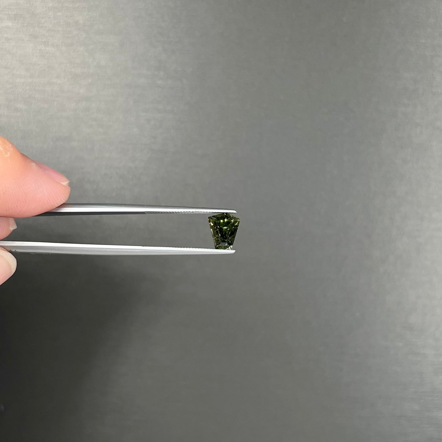 A loose, shield cut, natural moldavite gemstone.  The stone has a small chip in the top corner facet.