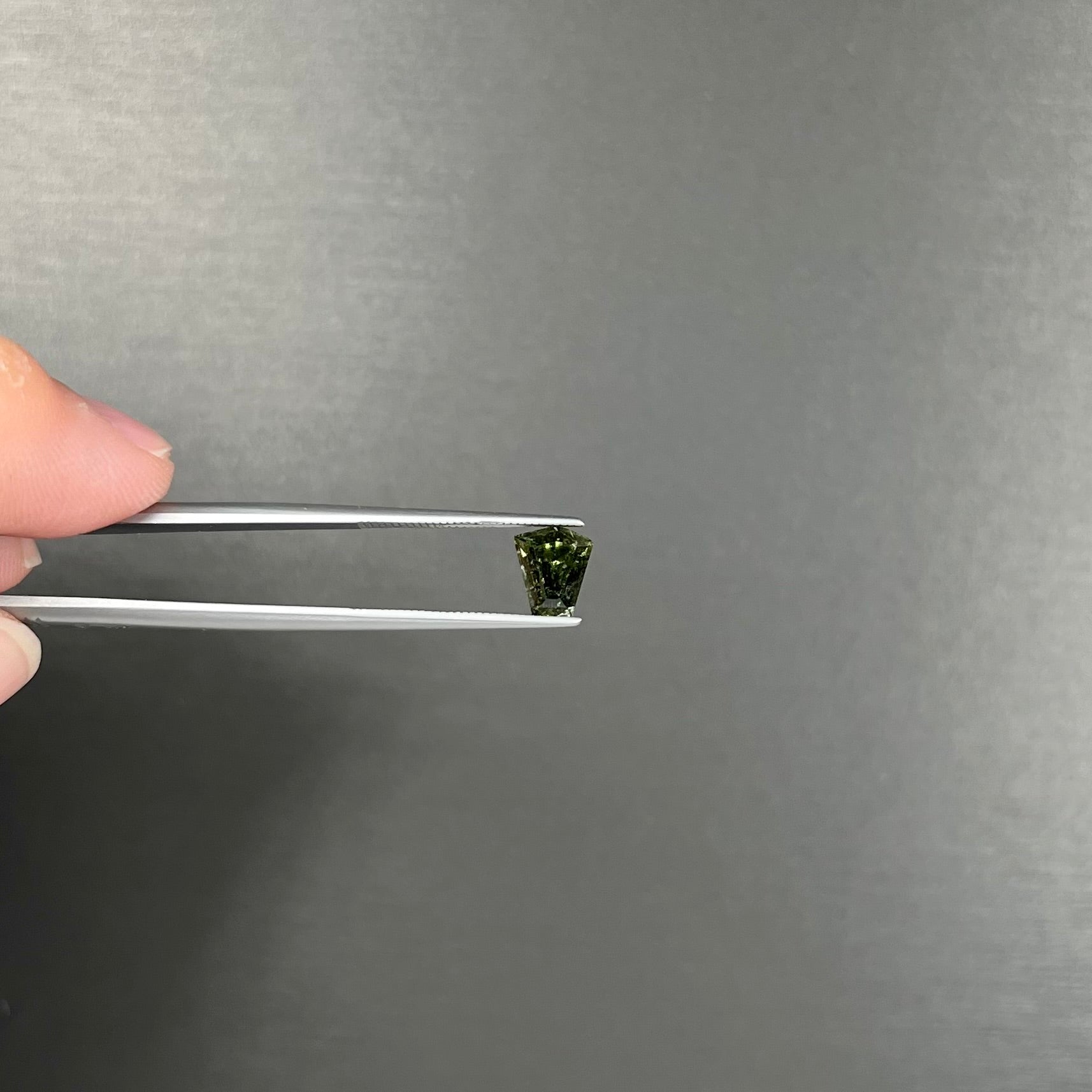 A loose, shield cut, natural moldavite gemstone.  The stone has a small chip in the top corner facet.