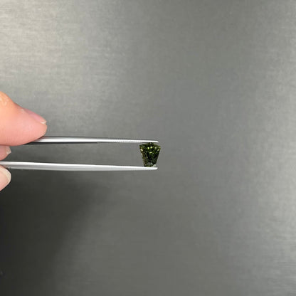 A loose, shield cut, natural moldavite gemstone.  The stone has a small chip in the top corner facet.