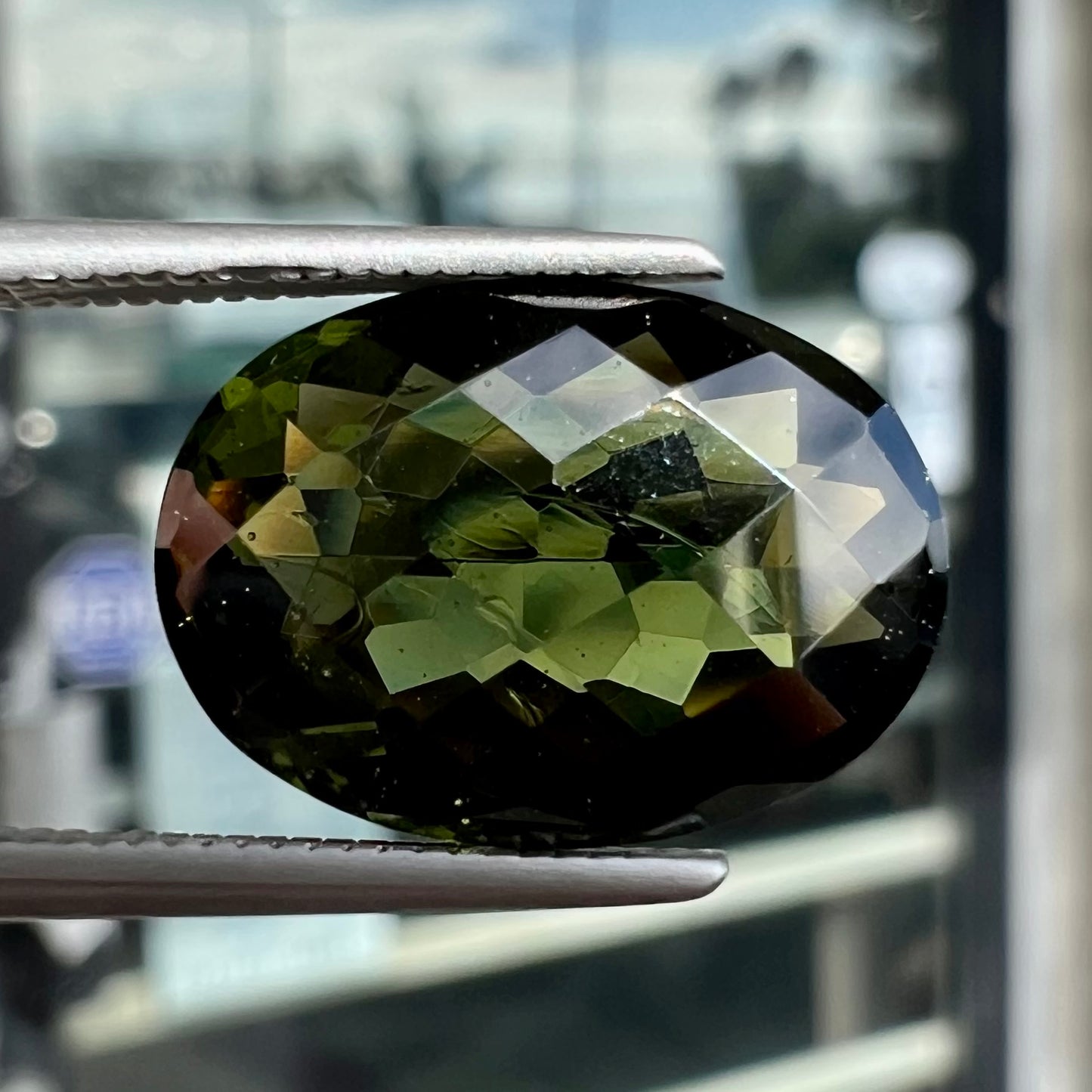 A faceted oval cut natural moldavite gemstone.